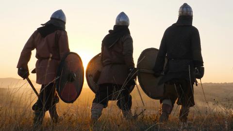 Three Viking warriors walking away from camera through a field